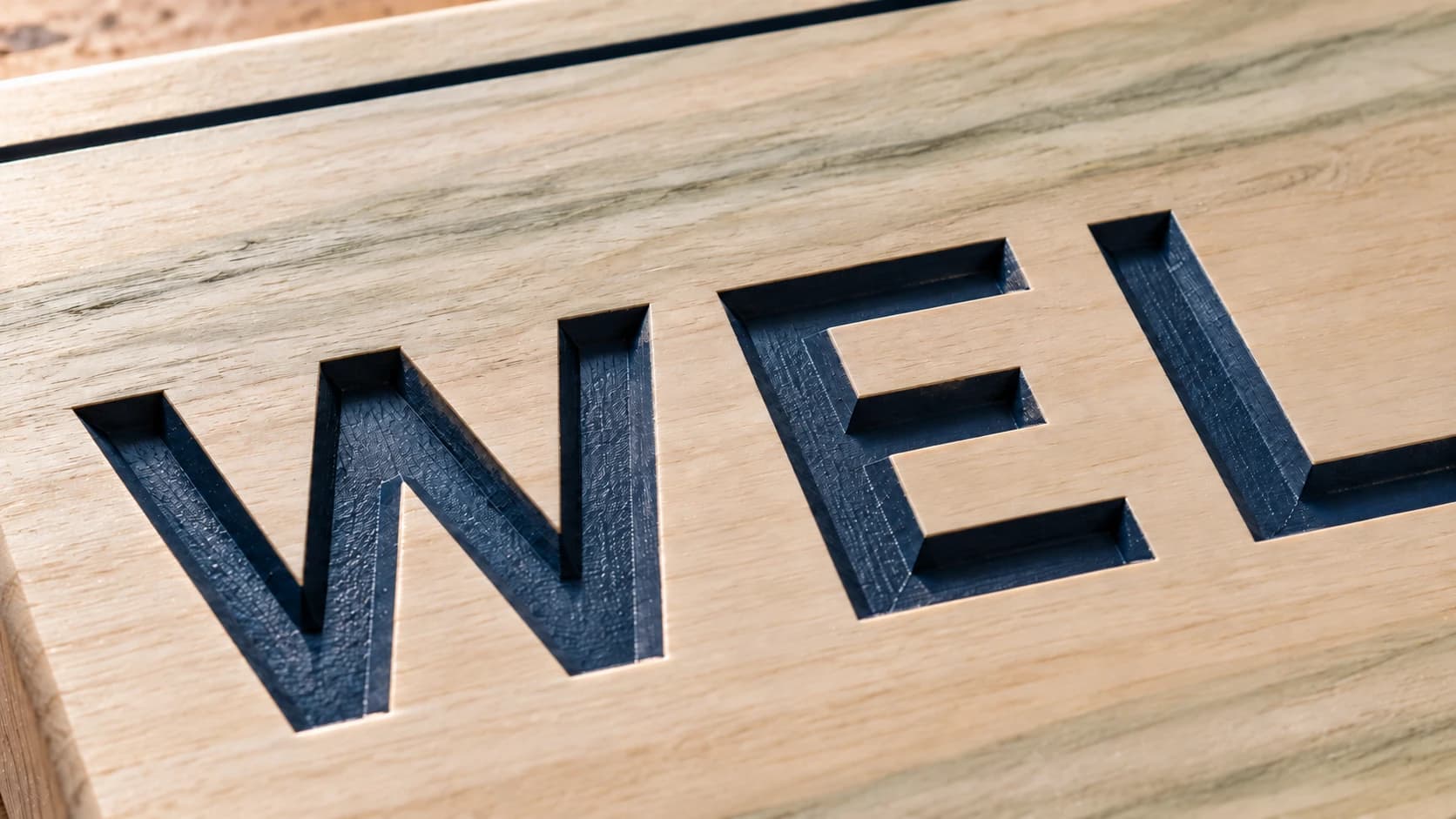 Navy paint inside recessed WELCOME lettering on poplar