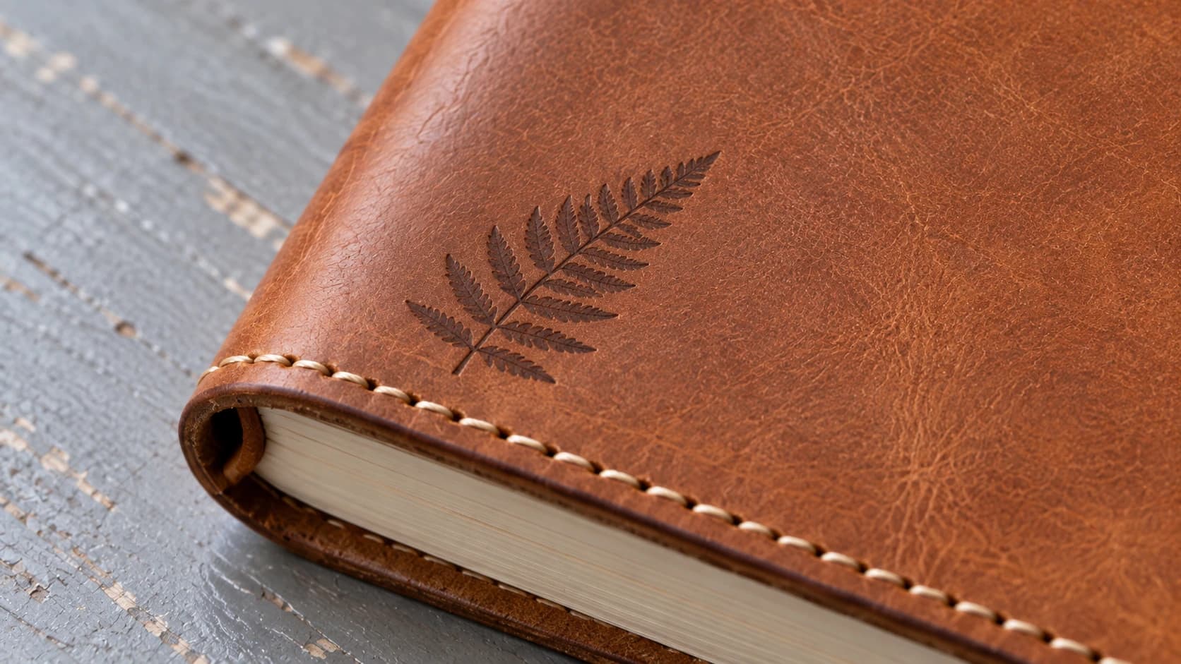 Close-up of a fern mark and saddle stitching on a tan leather notebook cover