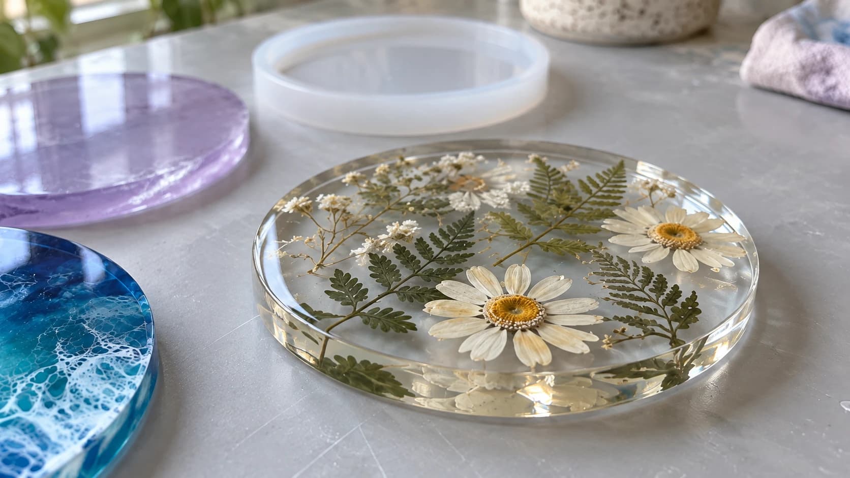 Sous-verre en résine transparente avec deux pâquerettes séchées et des feuilles de fougère entièrement incluses sous sa surface
