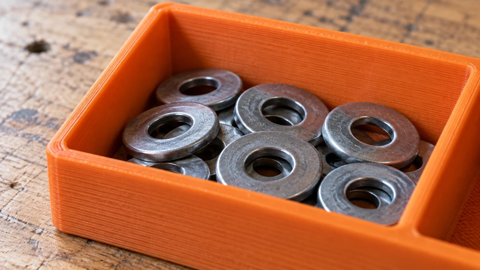 An orange printed tray compartment holding a small pile of steel washers on the worn workbench