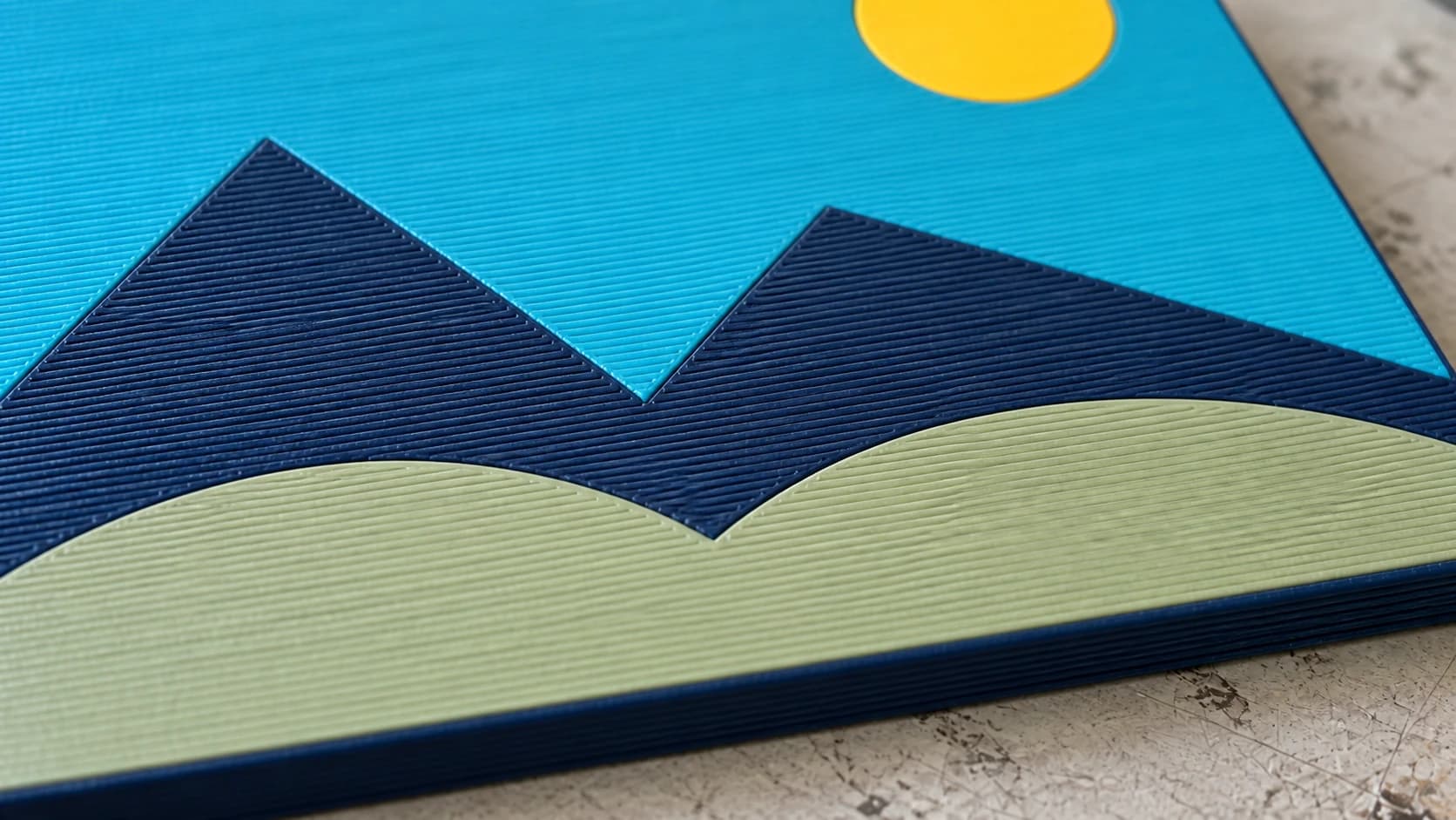 Close view of the printed landscape with adjacent turquoise, navy and sage filament regions meeting on a flat top surface
